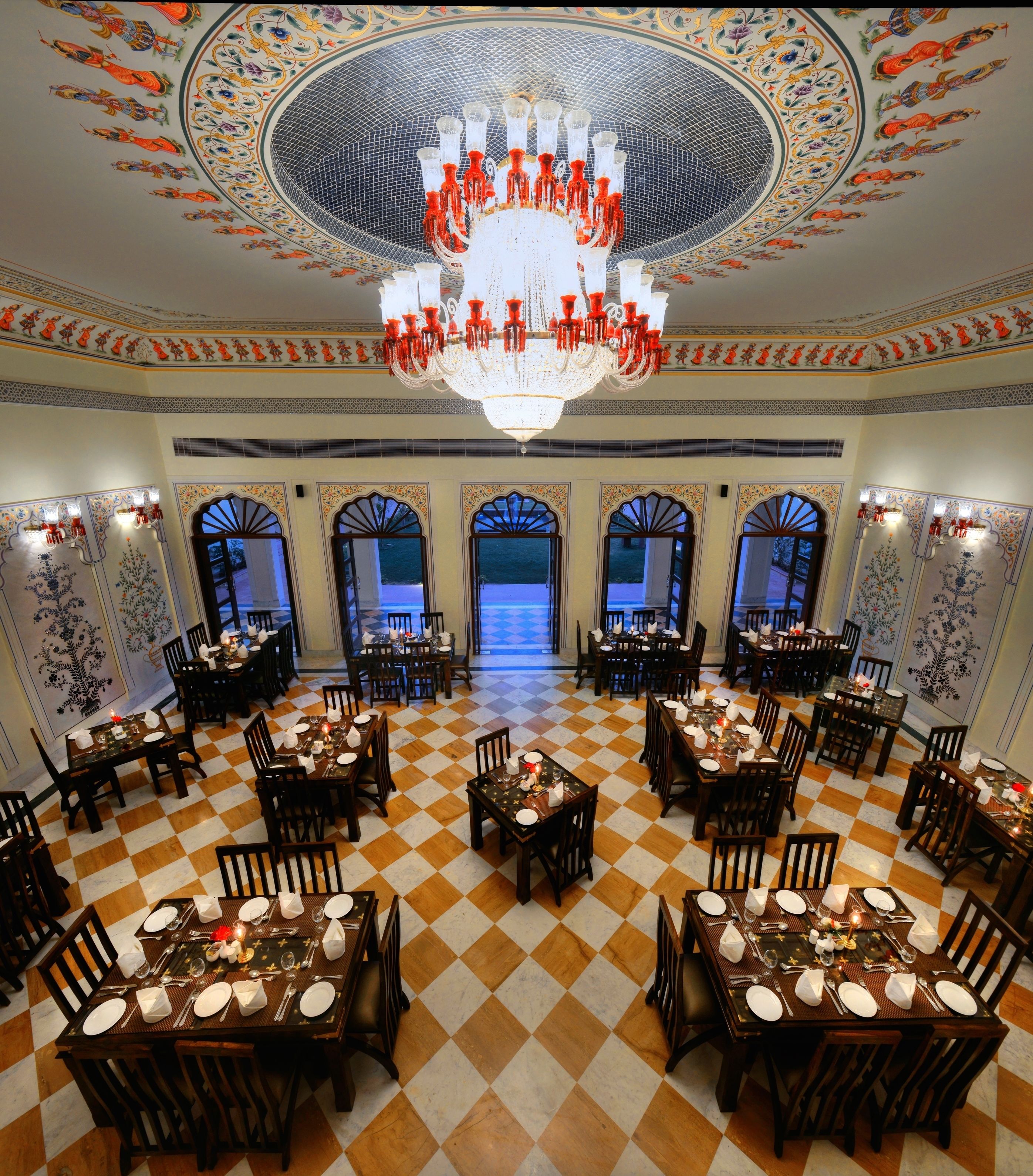 A dining area with checkered flooring, multiple tables set for dining, and a large chandelier.