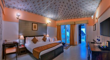Habitación de hotel con una cama grande, dos mesitas de noche con lámparas, un televisor y vistas al exterior.