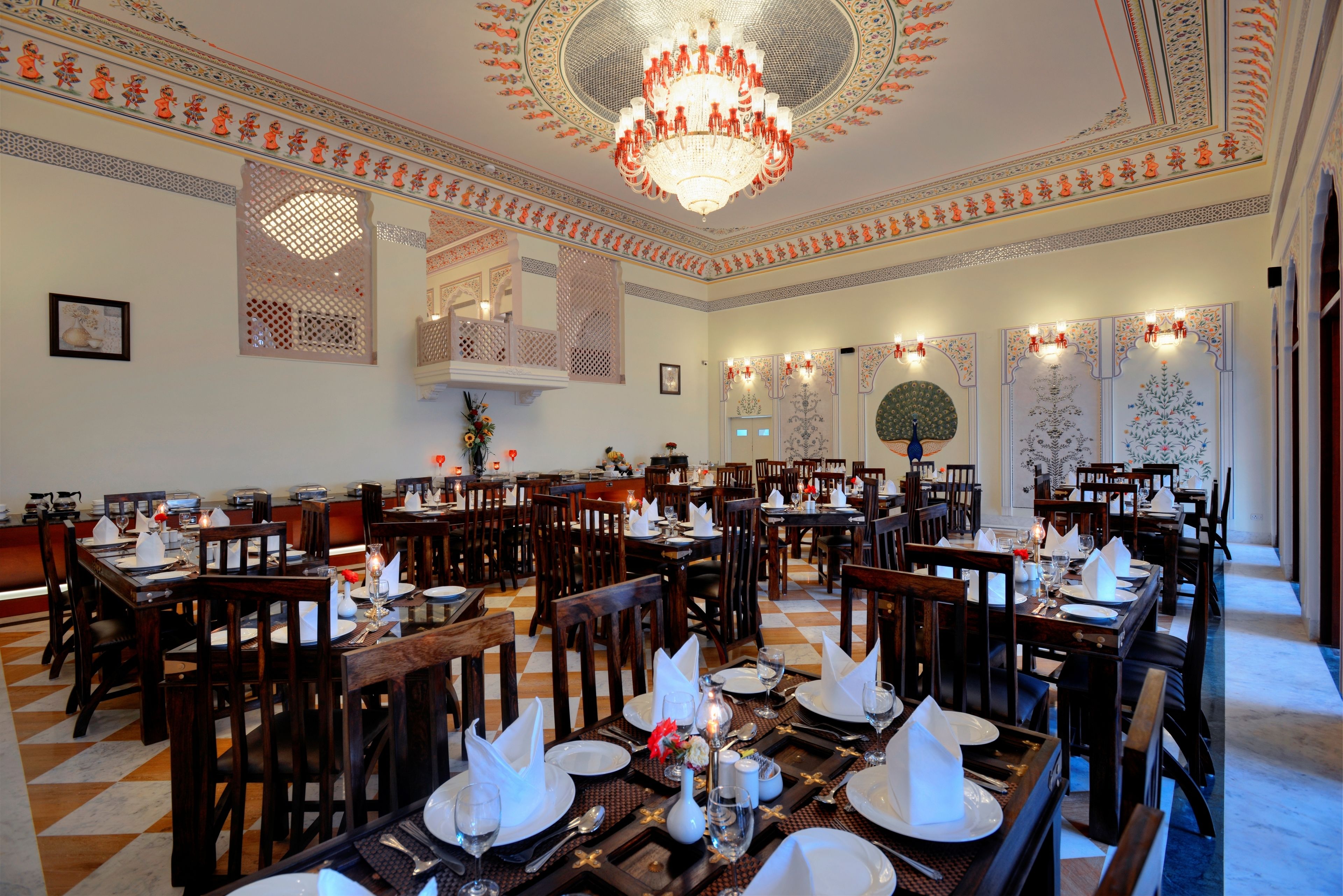 Un comedor con varias mesas dispuestas para el servicio, decoraciones ornamentales en el techo y un candelabro.