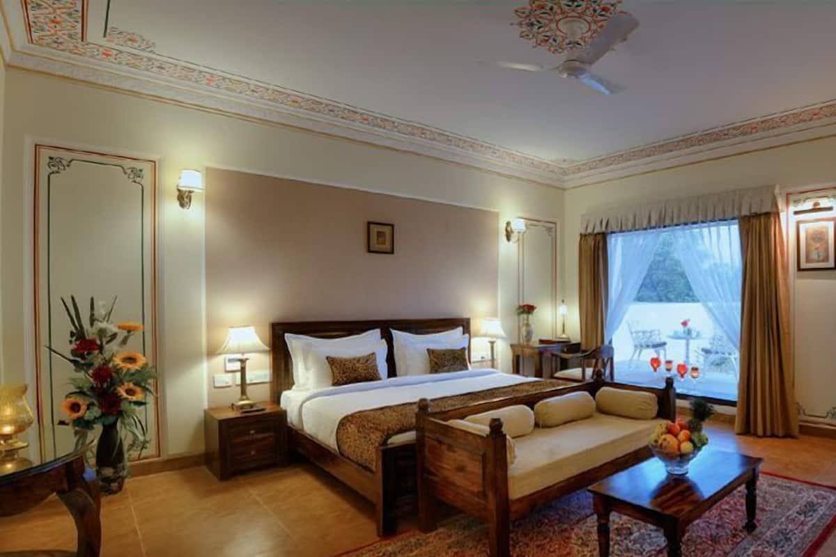 A well-appointed bedroom with a large bed, bedside lamps, a nightstand, a wooden bench, a coffee table, and a window with curtains.