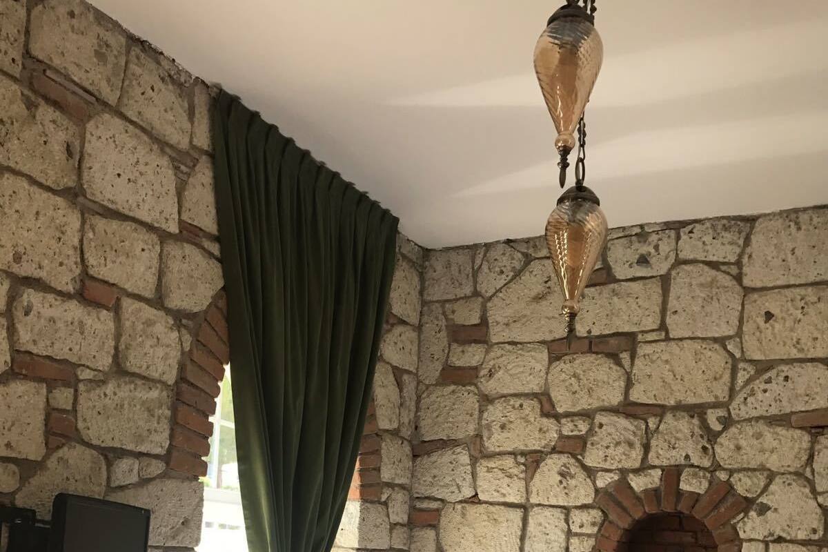 A room with a stone wall, a bed with white bedding, a green curtain, and a hanging light fixture.