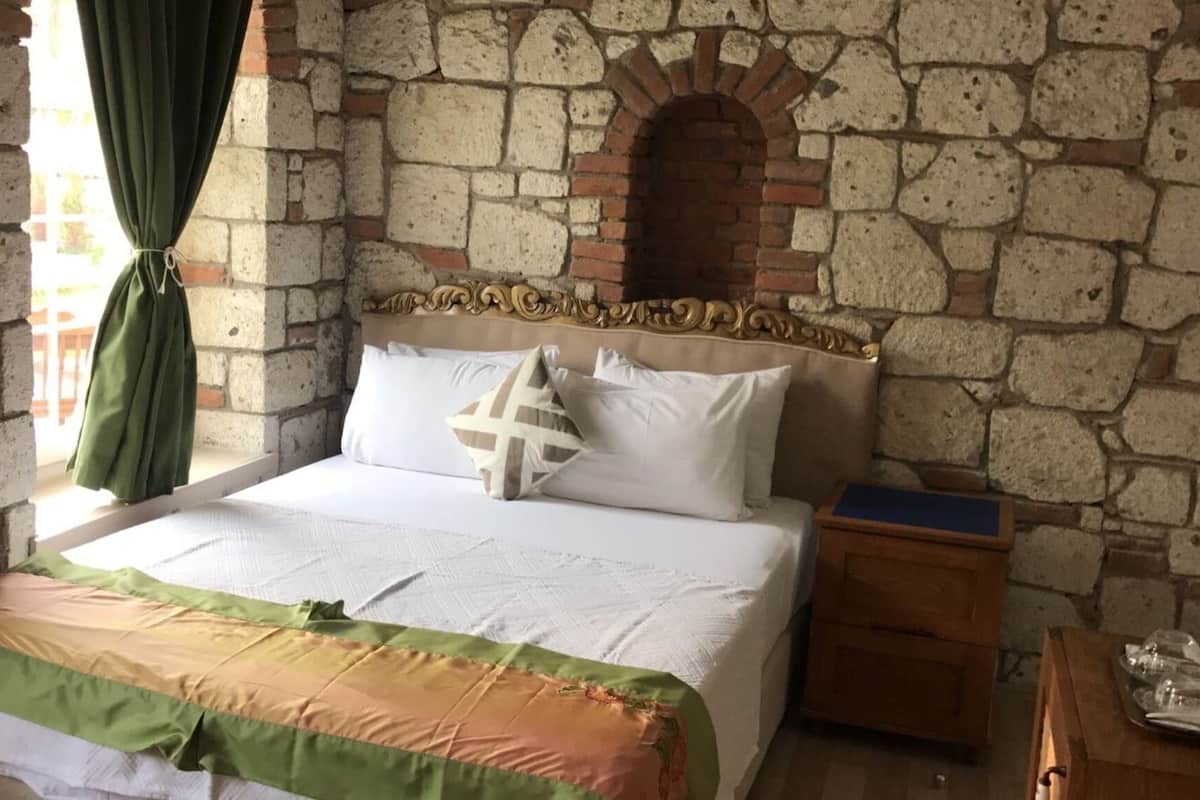 A bedroom with a stone wall, a bed with white bedding, a wooden nightstand, and a television on the wall.