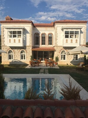 A large, two-story building with a tiled roof, a swimming pool, and outdoor seating. - Kerme Ottoman Alacati (Cesme)