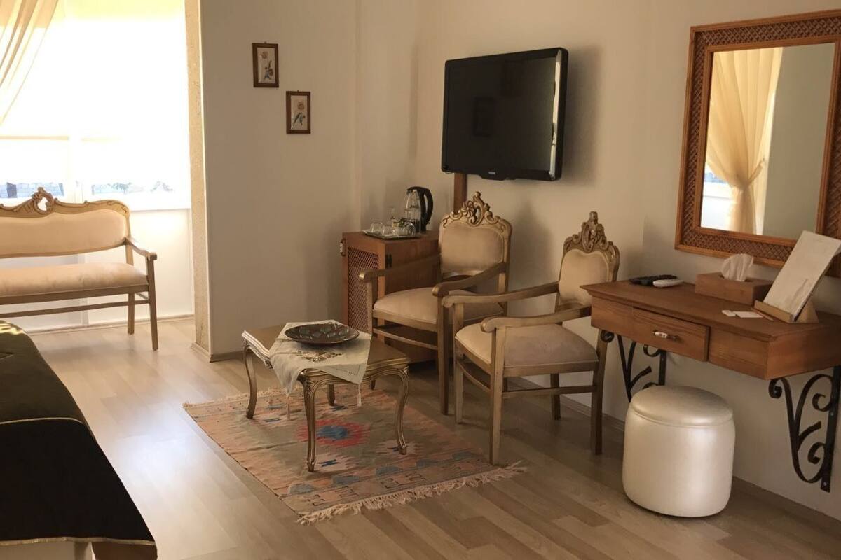 A bedroom with a bed, a desk, a chair, a television, and a window with curtains.