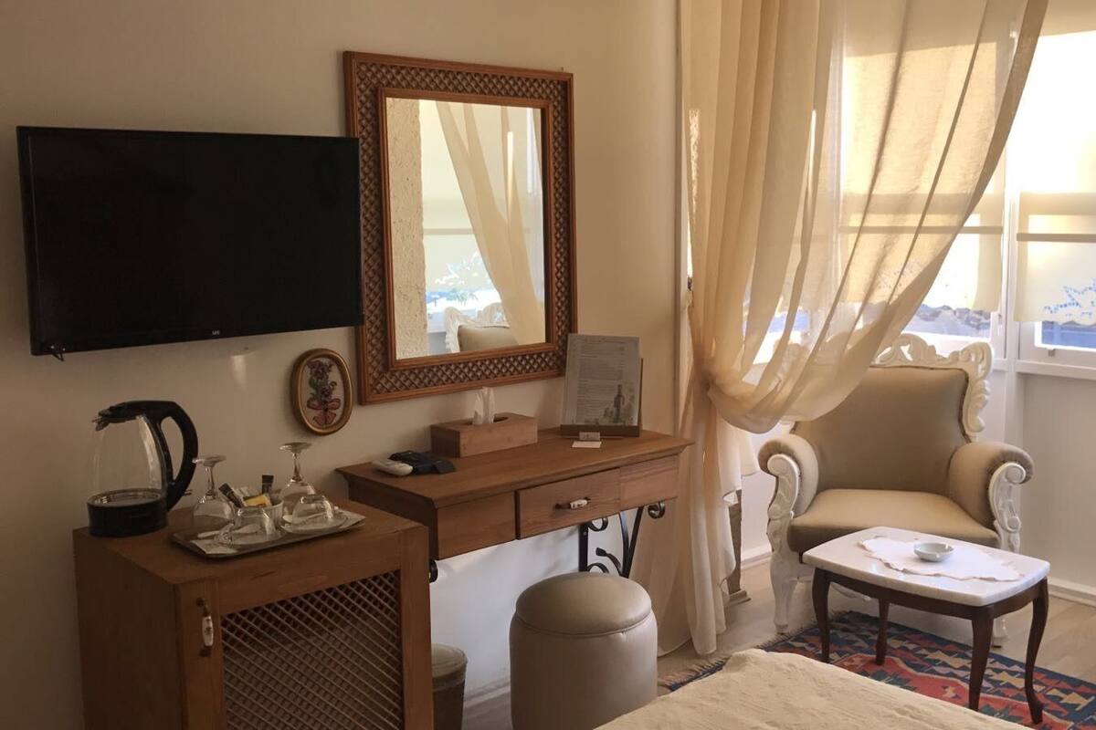 A hotel room with a wooden desk, a television, a comfortable armchair, and a view of the mountains through the window.
