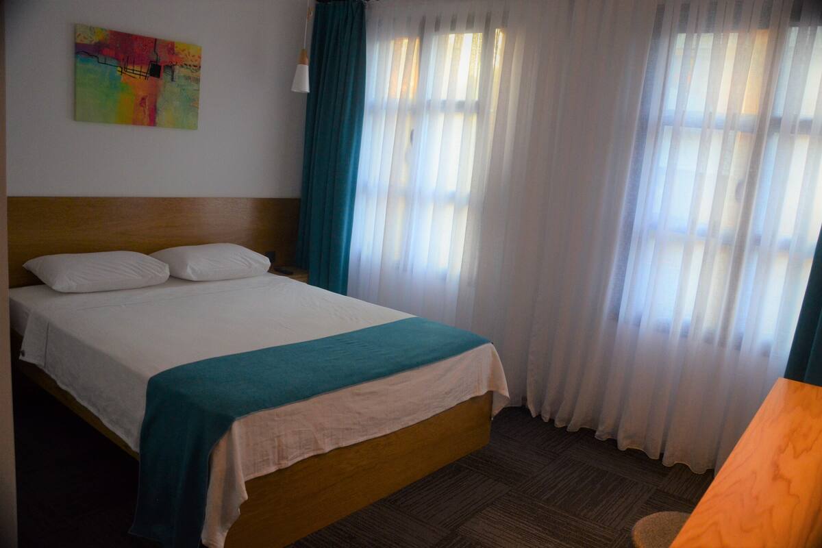 A hotel room with a bed, curtains, and a painting on the wall.
