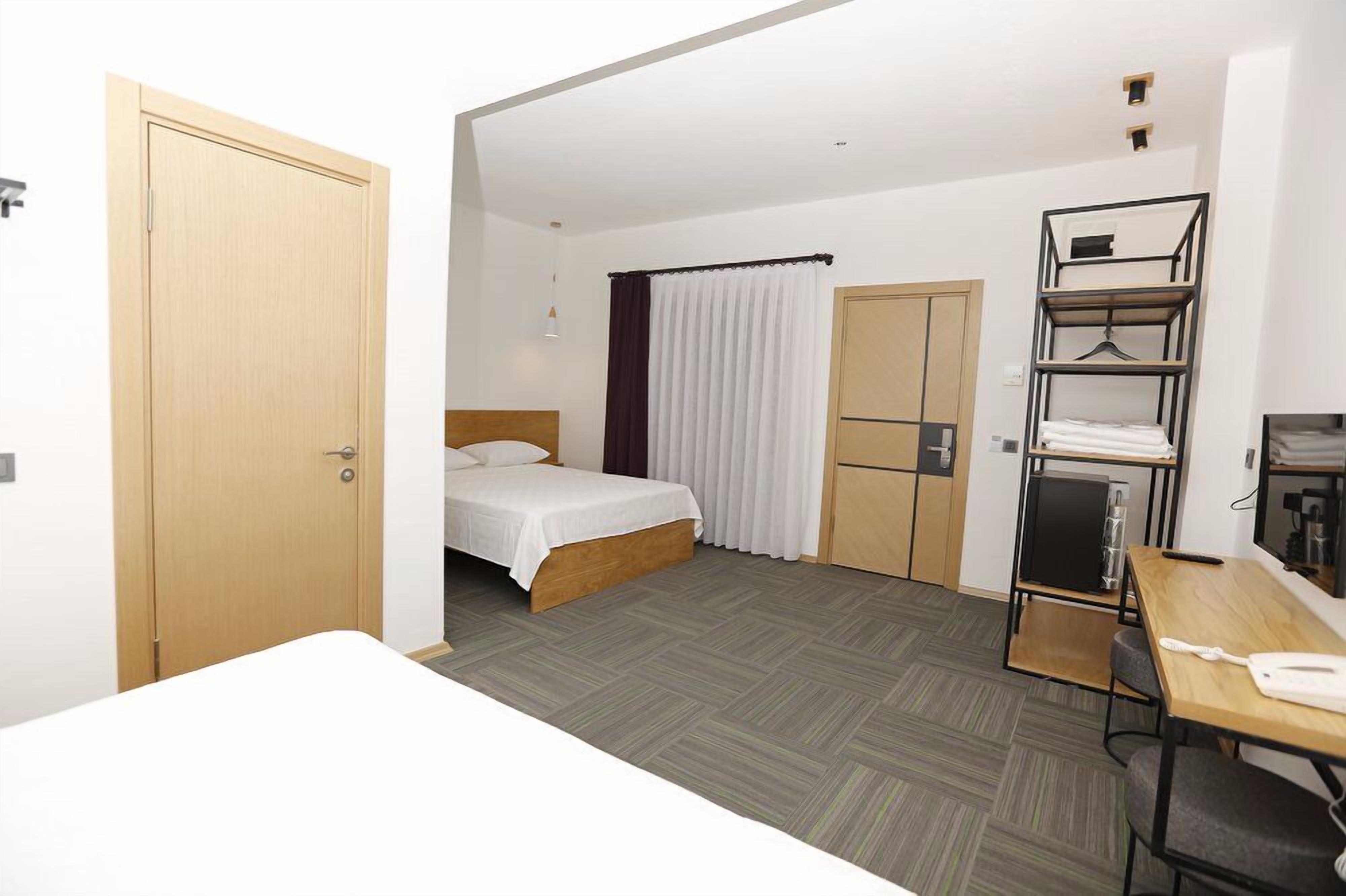 A compact hotel room with a bed, a desk, a wardrobe, and a shelf unit.