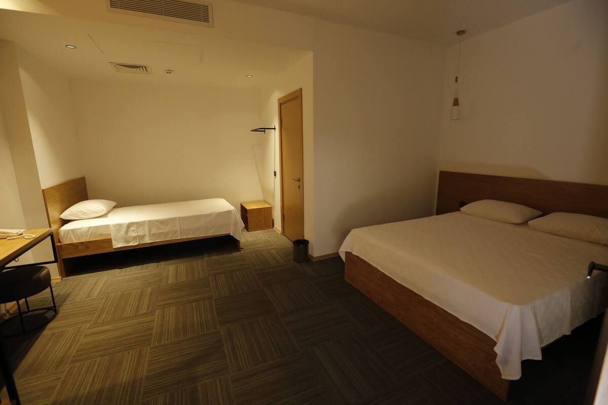A hotel room with a large bed, a smaller bed, a desk, and a chair.