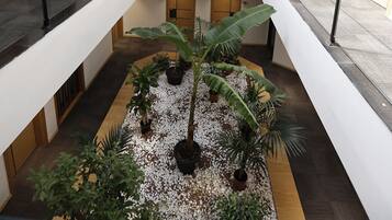 Um átrio amplo em vários níveis, com jardim central, guarda-corpos de vidro e teto curvo.