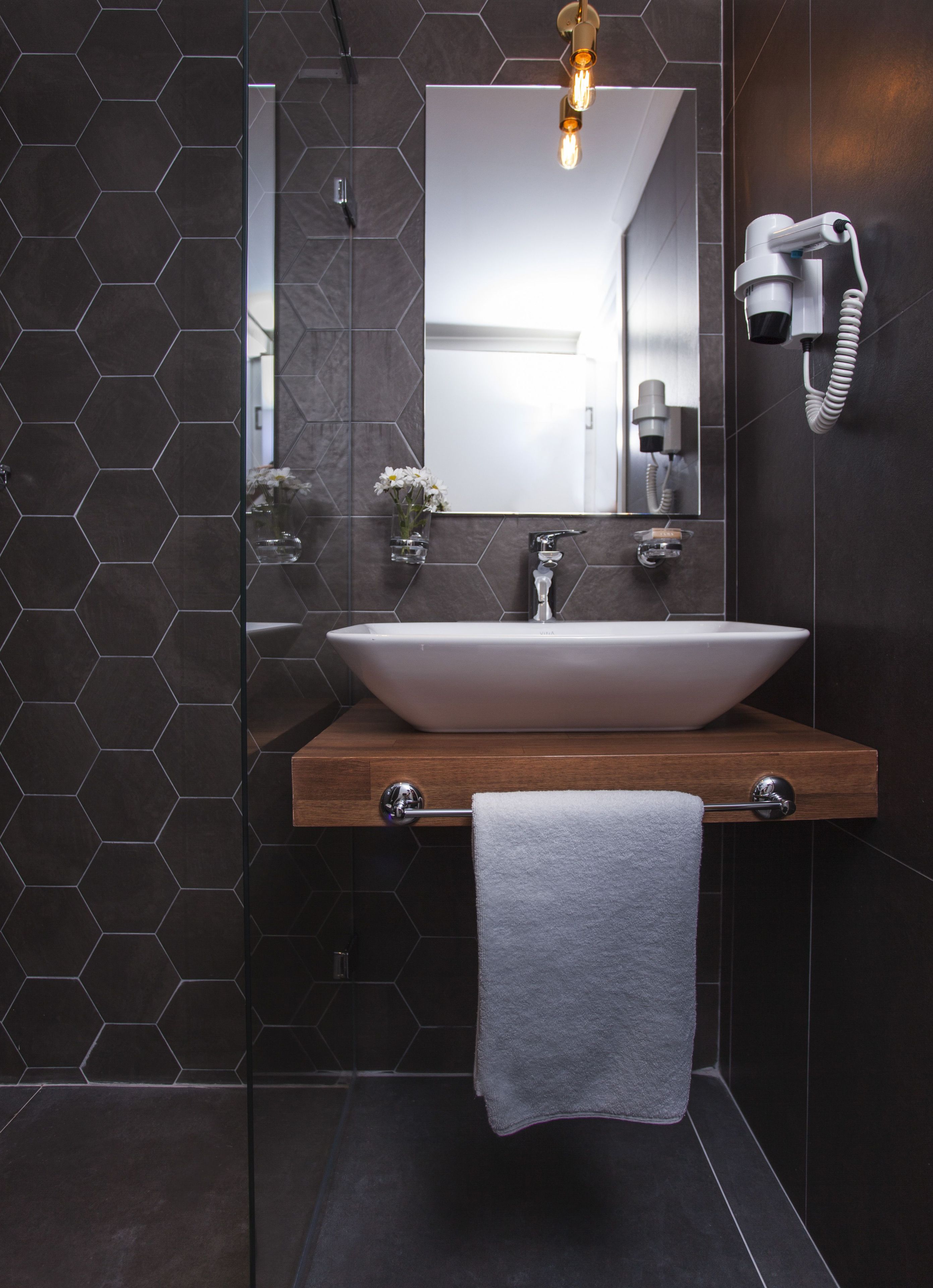 A modern bathroom with a large vessel sink, a wooden countertop, a towel rack, and a hairdryer mounted on the wall.