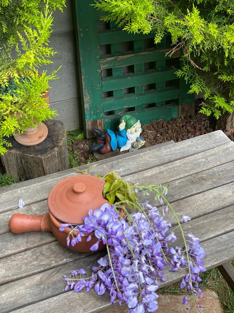 Entorn rústic a l'aire lliure amb una banca de fusta, una olla de fang i flors morades.