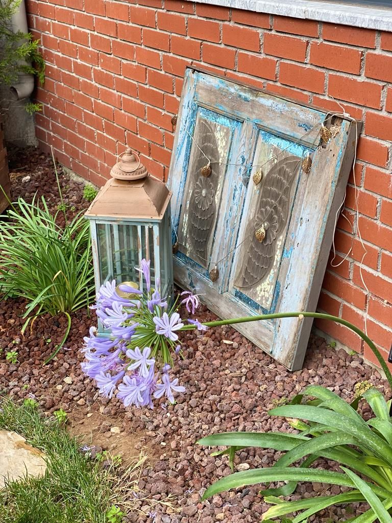 A rustic outdoor setting with a brick wall, a vintage lantern, and purple flowers.