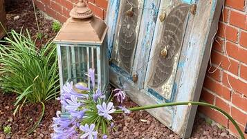 A rustic outdoor setting with a brick wall, a vintage lantern, and purple flowers.
