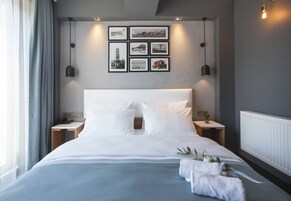 A neatly made bed with white linens, a bedside table with a lamp, and a wall with framed pictures.