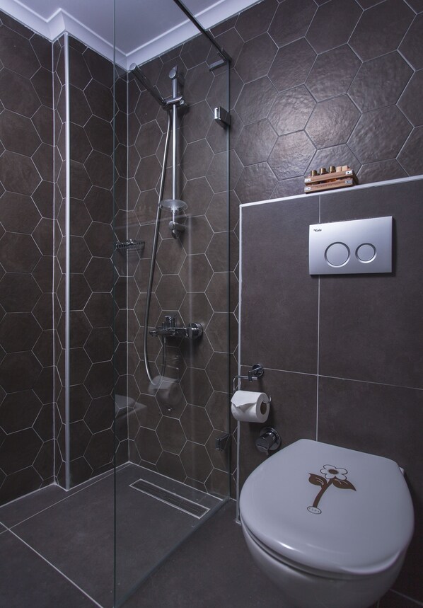 Un baño moderno con pared de azulejos hexagonales, cabina de ducha de vidrio, inodoro con diseño floral y panel de control empotrado.