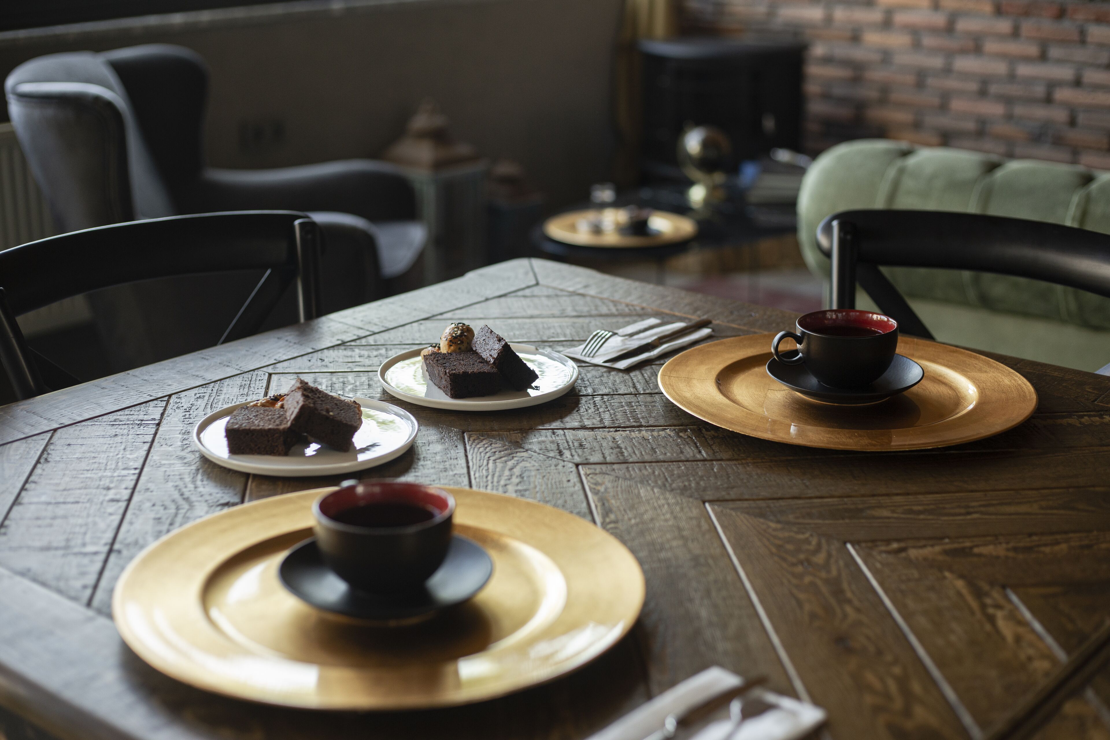 Une table en bois, sur laquelle sont disposées des assiettes de nourriture et une tasse, se trouve dans une pièce aux murs de briques et meublée dans un style moderne.