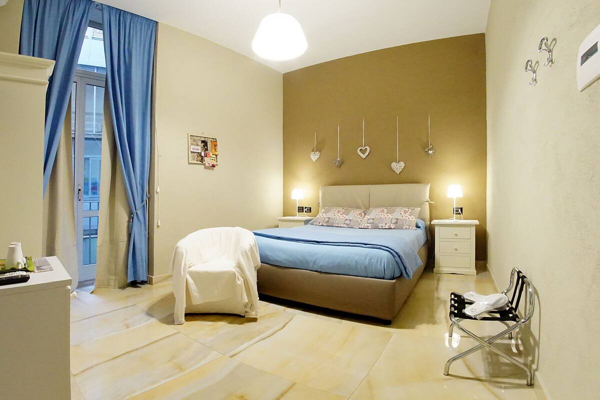 A bedroom with a bed, bedside tables, a chair, a desk, and a TV.