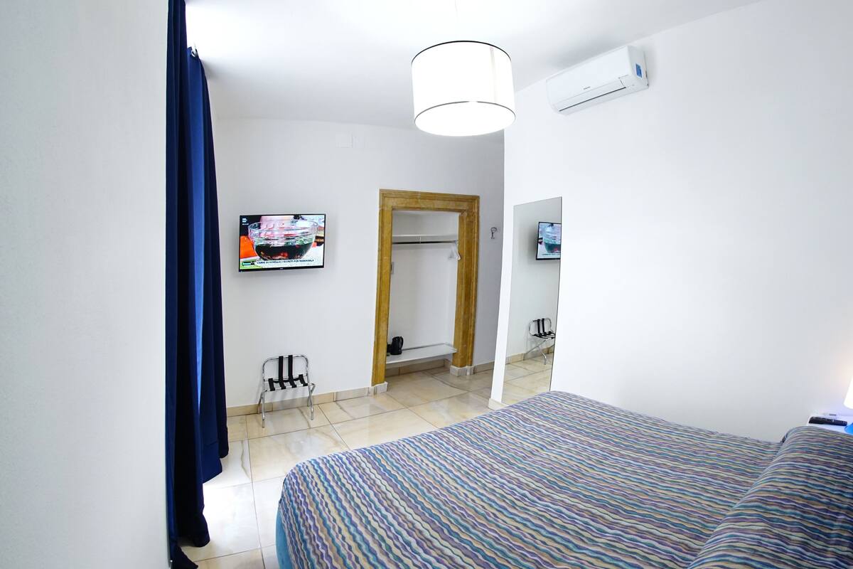 A hotel room with a bed, a television, an air conditioning unit, and a mirror.