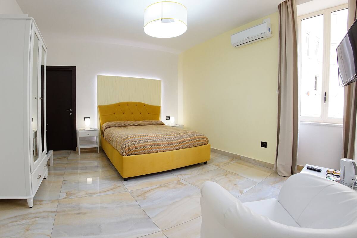 A hotel room with a bed, a wardrobe, a desk, a chair, and a window with curtains.
