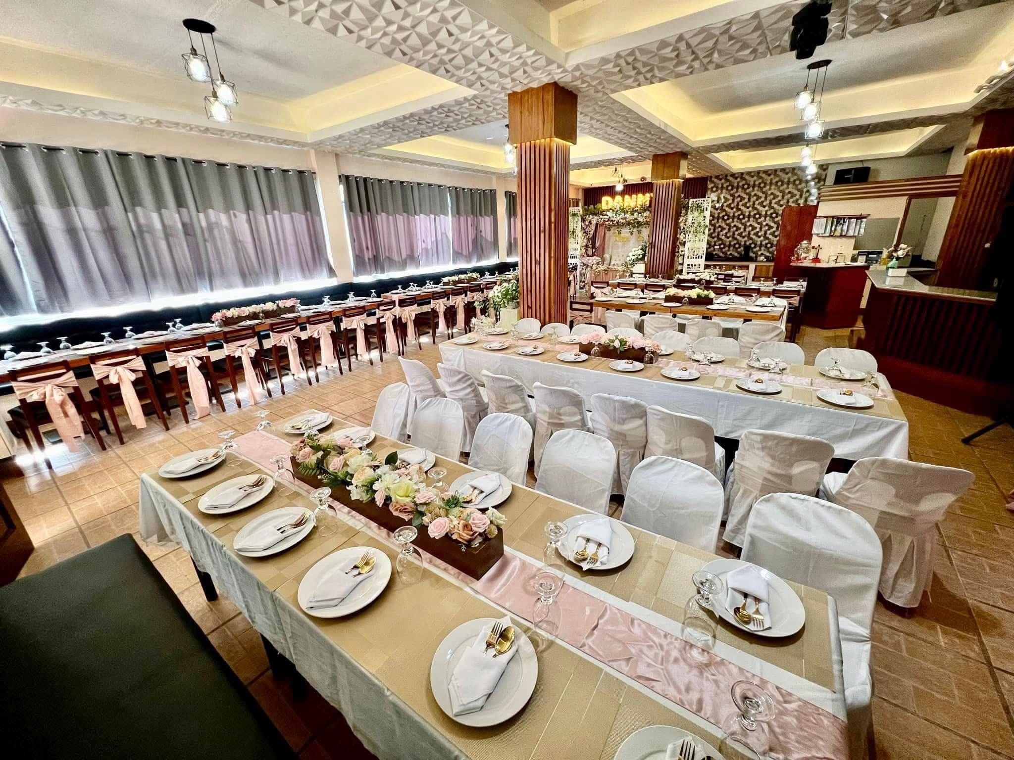Un salón de banquetes con varias mesas largas dispuestas para cenar, sillas blancas y un techo decorativo.