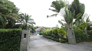 A gated entrance with a paved driveway leading to a house surrounded by lush tropical vegetation.