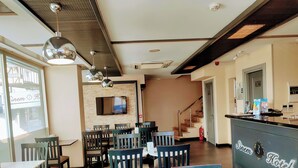 Un vestíbulo de hotel con mostrador de recepción, varias áreas de estar, un televisor montado en la pared y una escalera que conduce a un nivel superior.