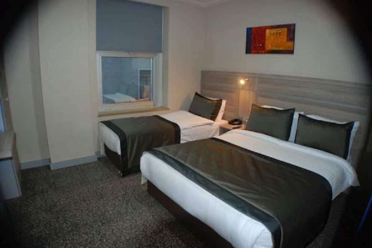 A hotel room with two beds, a window, a nightstand, and a wall-mounted lamp.