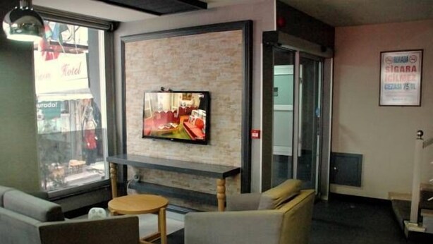 Un vestíbulo con una televisión montada en una pared de ladrillo, zona de estar con sofás y una mesita, y un ventanal con vista a la calle.