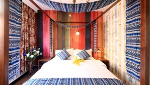 A room with a bed, curtains, a chandelier, and a vase with flowers.