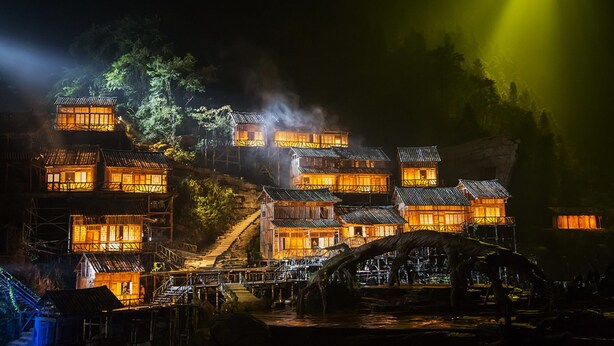 A traditional wooden building with multiple levels, connected by staircases, and illuminated by warm lighting.