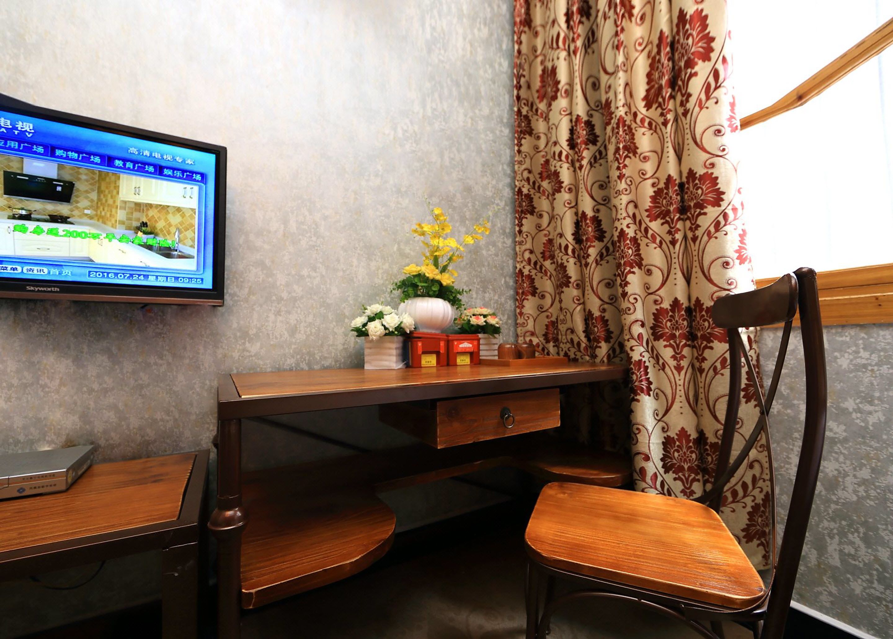 Habitaci ón de hotel con un escritorio de madera, un televisor montado en la pared, un arreglo floral y una silla.