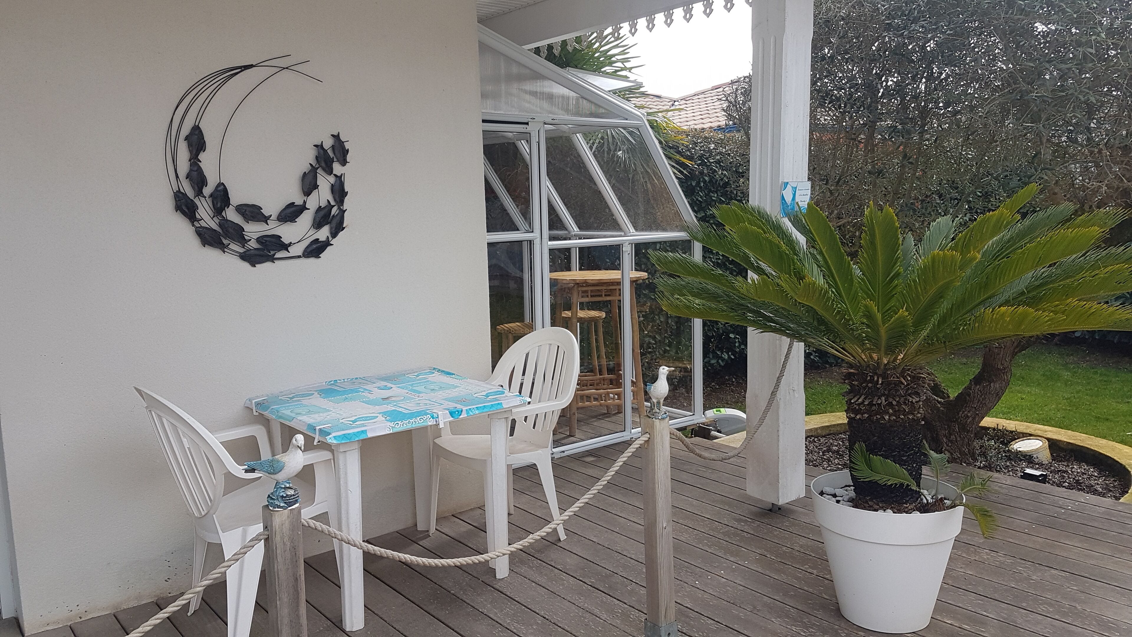 A covered outdoor seating area with a table and chairs, a potted plant, and a decorative wall piece.