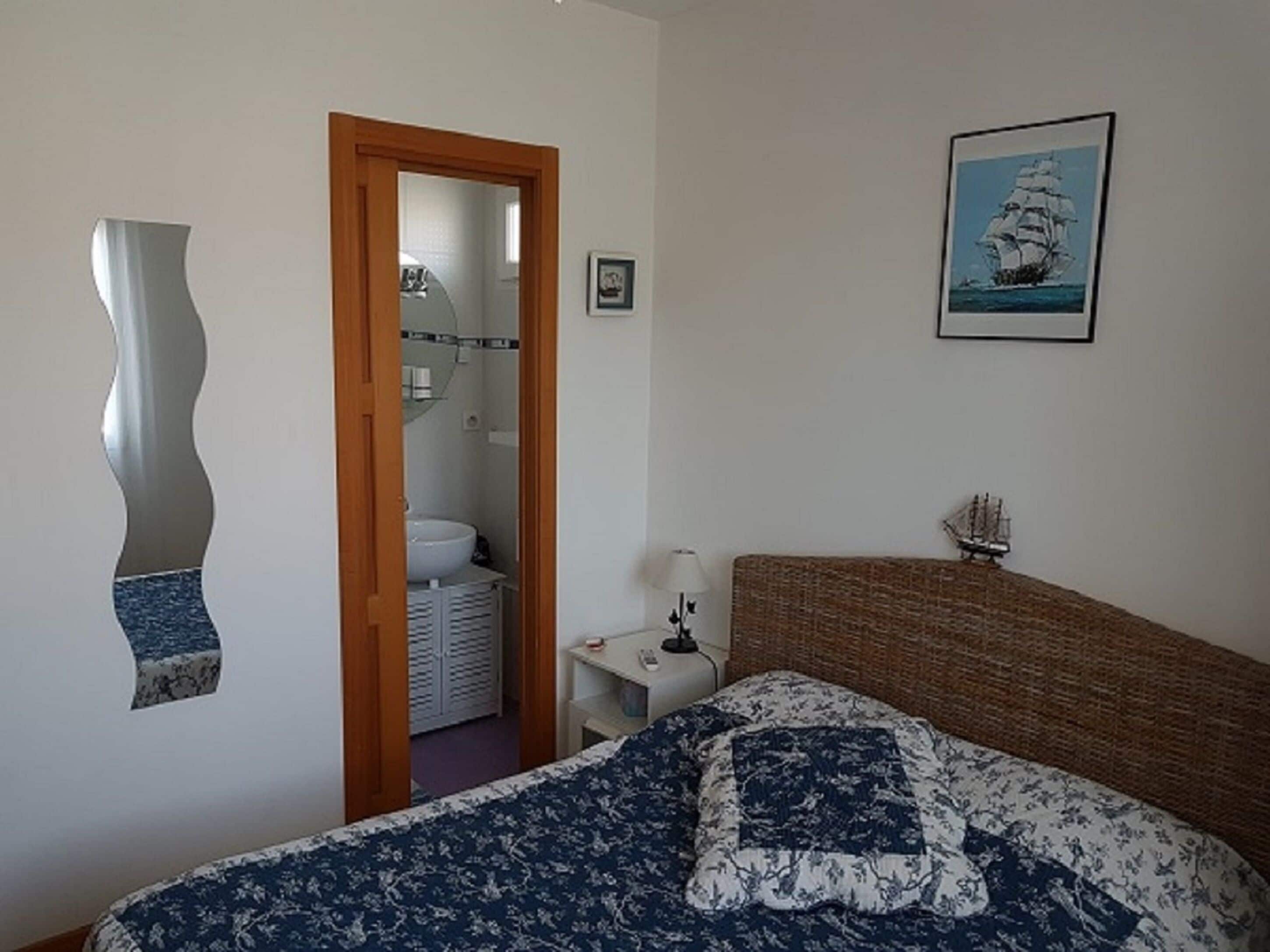 A bedroom with a bed, a nightstand, a lamp, a mirror, and a framed picture on the wall.