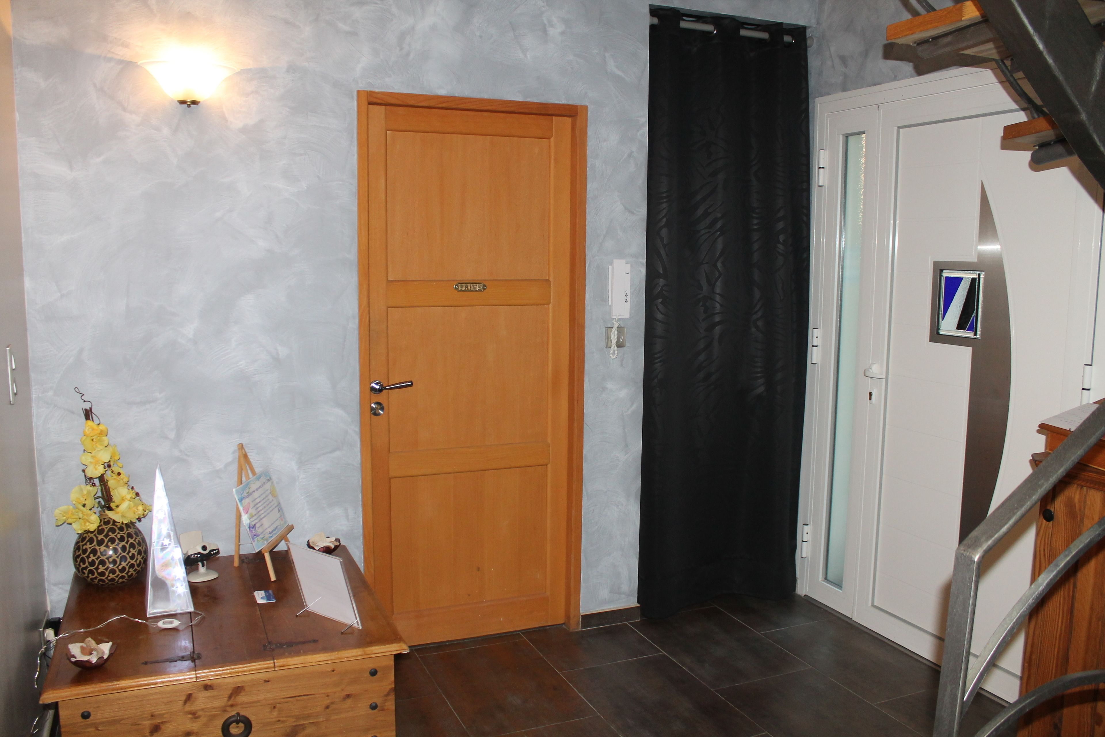 A wooden door with a handle, a black curtain, and a white door with a small blue and white sign.