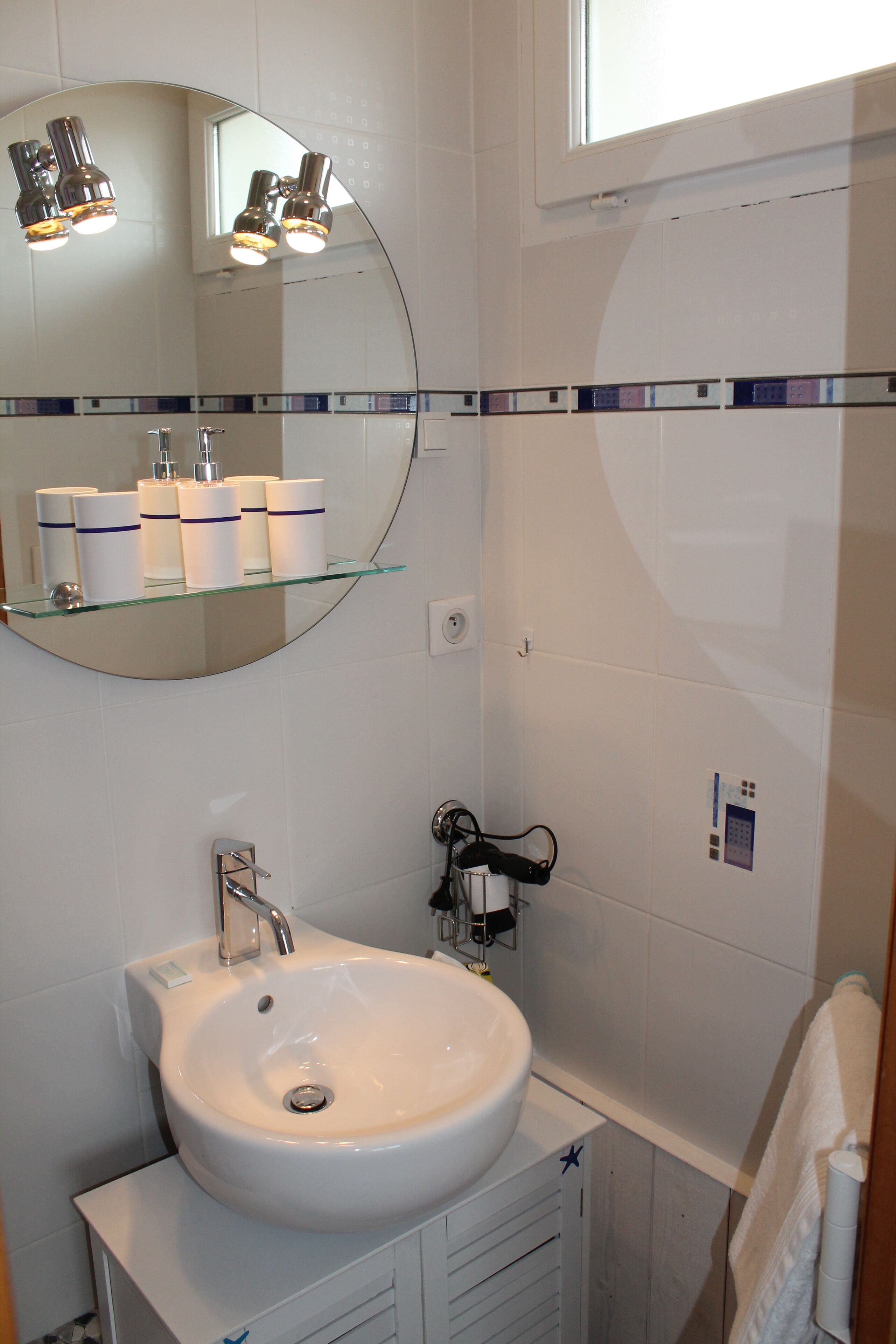 A bathroom with a white sink, a glass shelf with toiletries, a mirror, and a window.