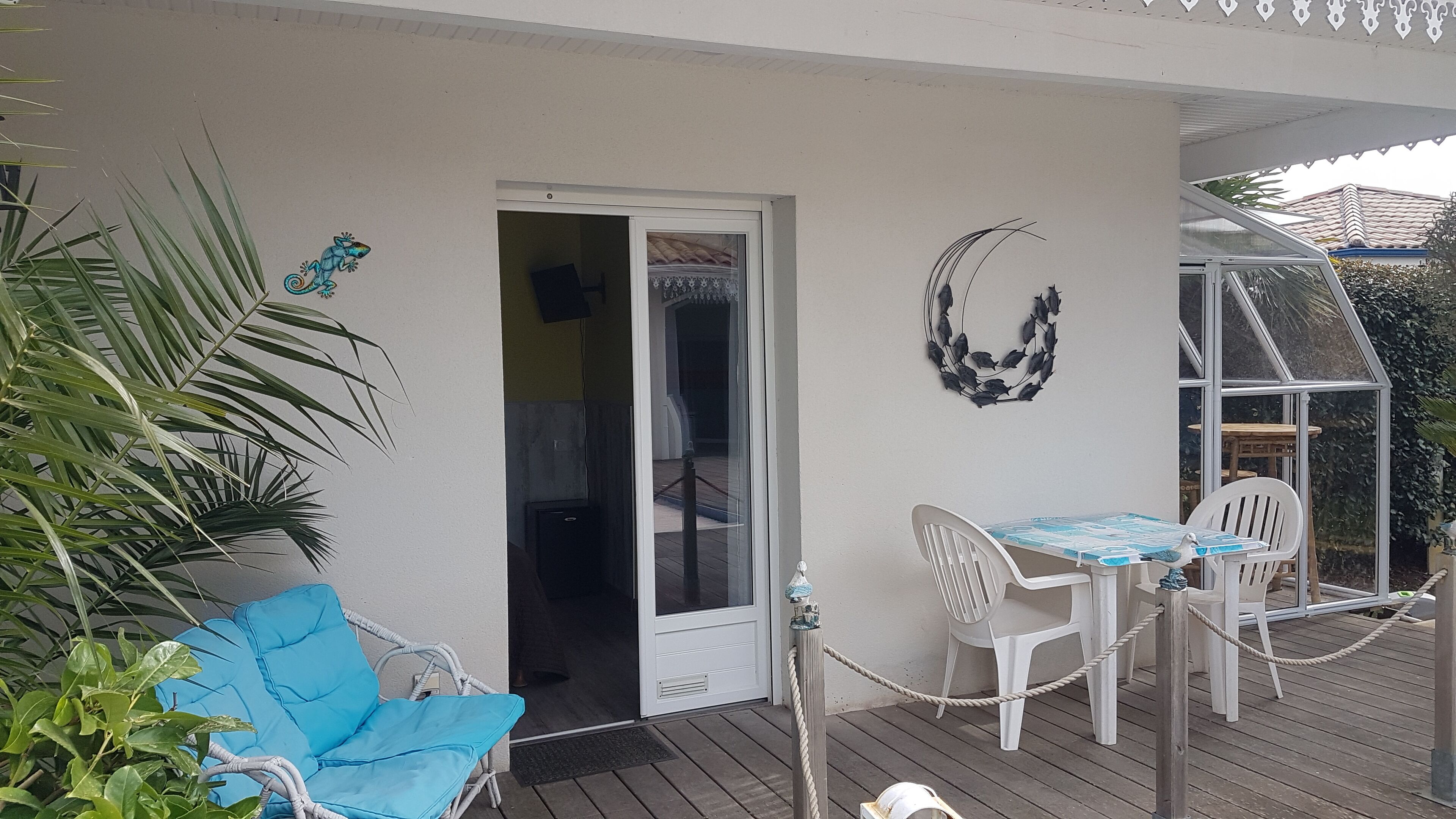 Un espacio al aire libre techado con mesa y sillas, una puerta que da a un espacio interior y decoración en las paredes.