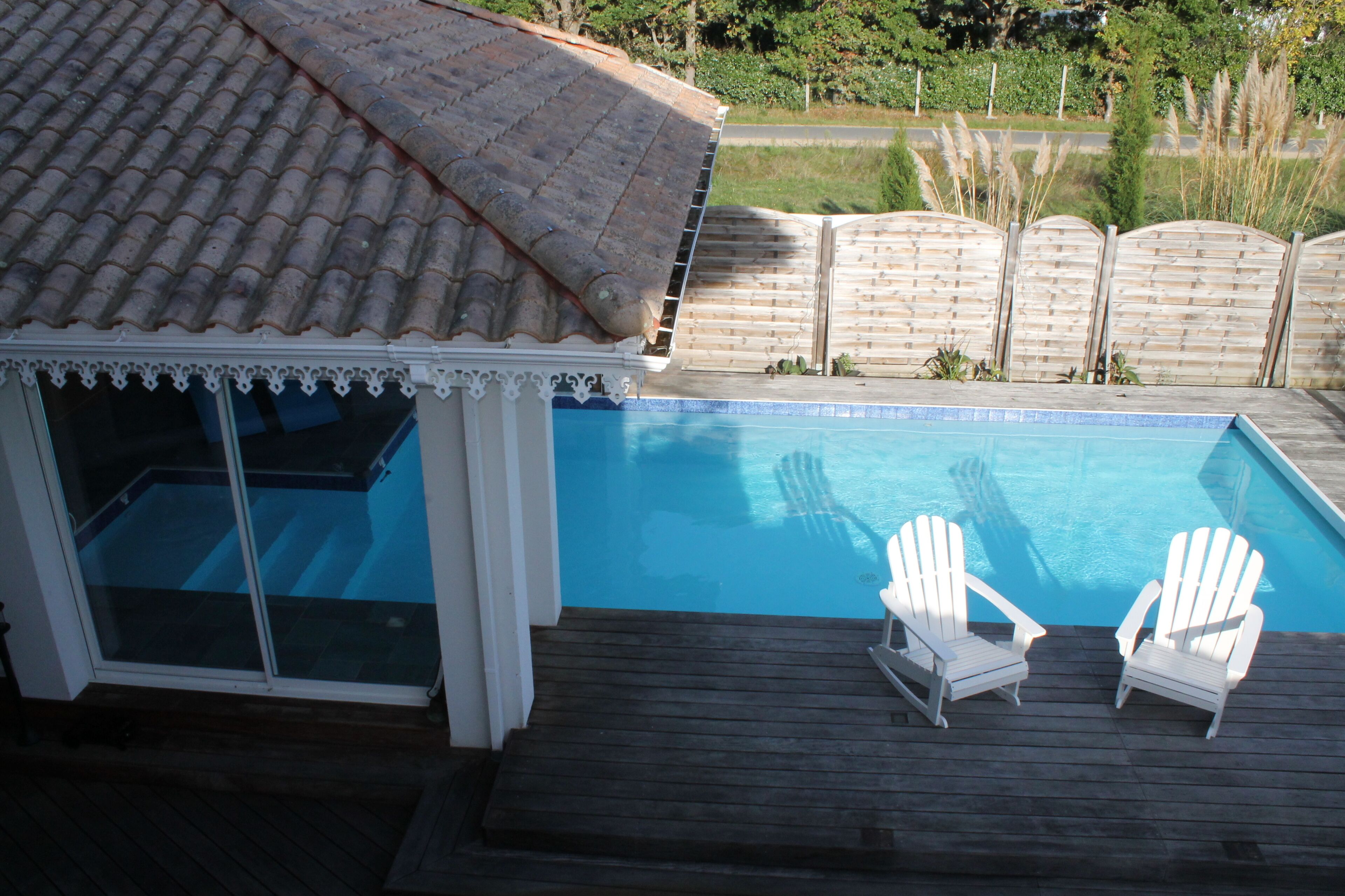 A swimming pool with two white Adirondack chairs on a wooden deck.
