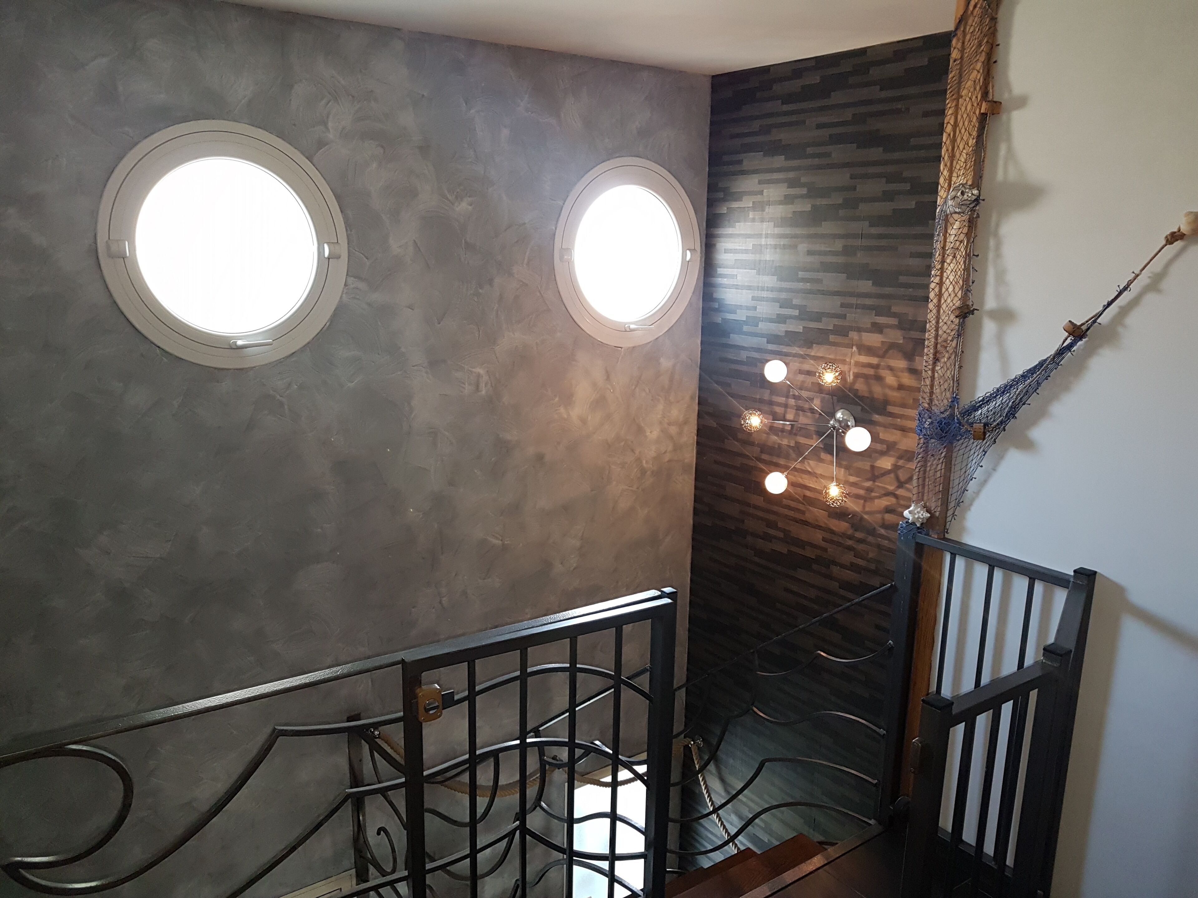 A staircase with a metal railing, two circular windows, and a wall with a textured pattern.