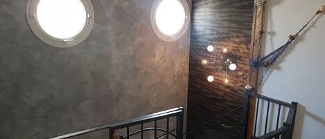 Una escalera con barandilla de metal, dos ventanas circulares y una pared con textura.