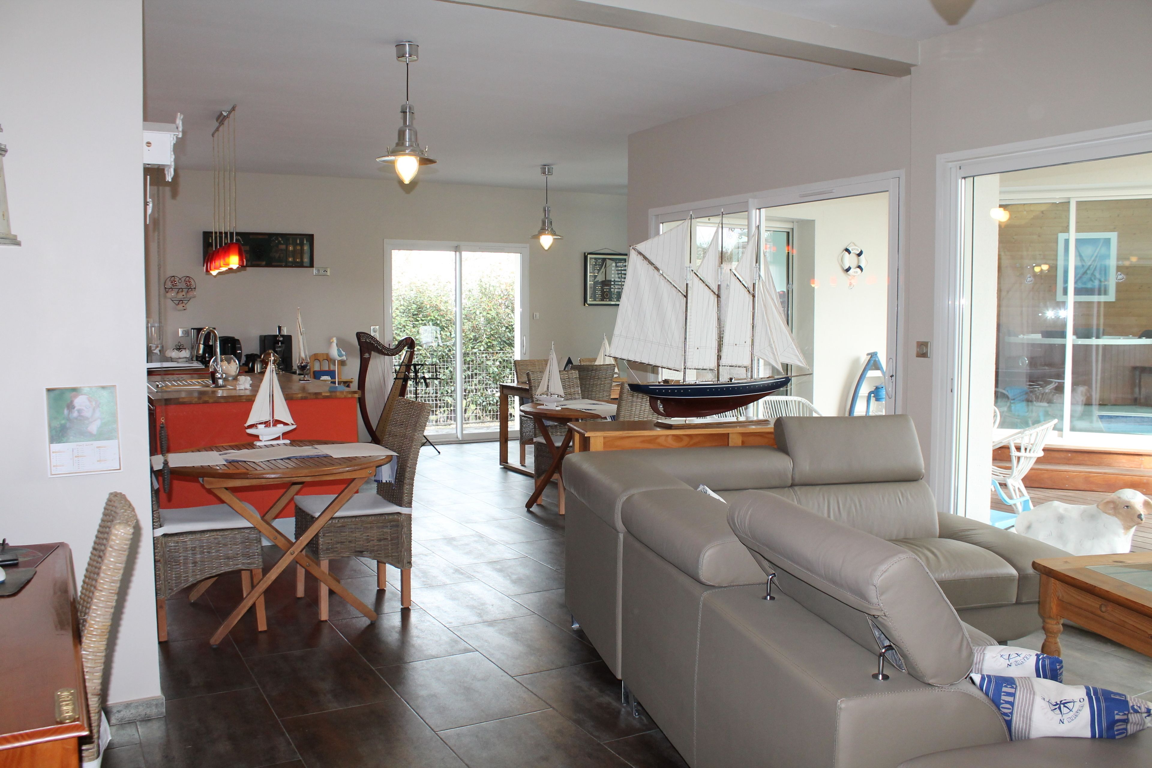 A spacious living room with a large sofa, a dining area with a table and chairs, and a kitchen in the background.