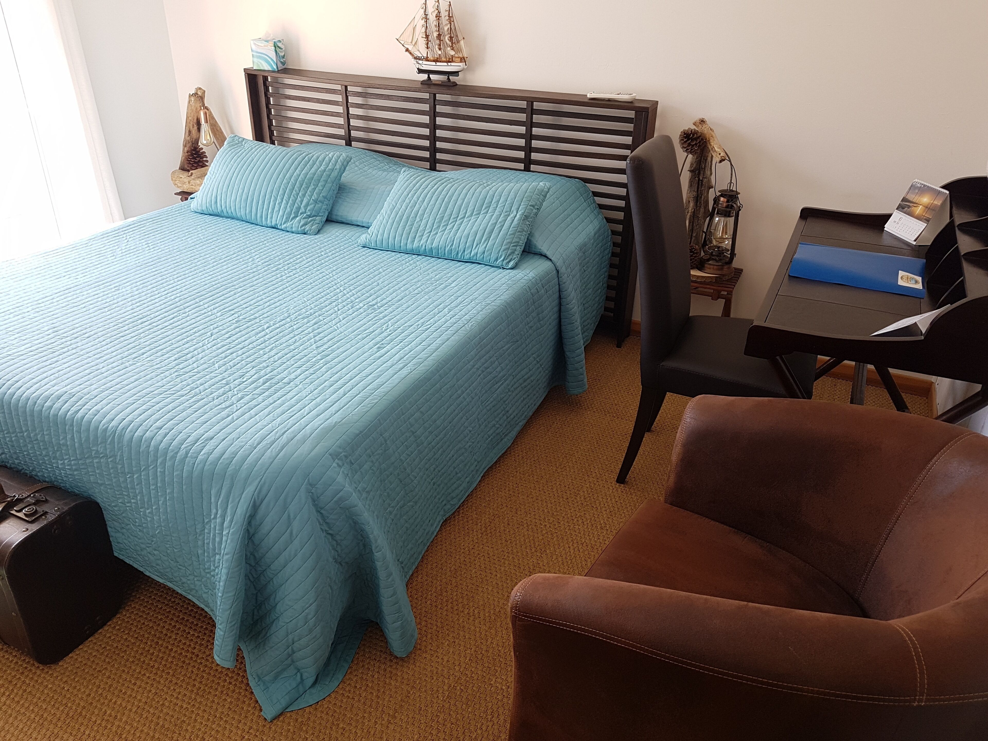 Un dormitorio ordenado con una cama grande, un escritorio y una silla.