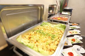 Un bufé con diversos platos, incluyendo ensaladas, carnes y una bandeja grande de verduras mezcladas.