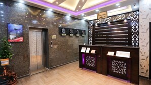 A reception area with a reception desk, a sign indicating the reception, a wall-mounted clock, and a potted plant. - 7Boys Hotel (Amman)
