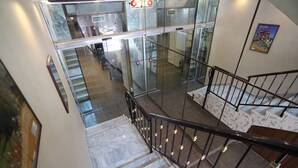 A staircase with a glass elevator door, marble steps, and a black metal railing. - 7Boys Hotel (Amman)