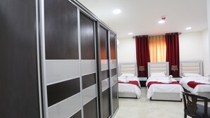 A hotel room with two beds, a wardrobe, and a chair. - 7Boys Hotel (Amman)