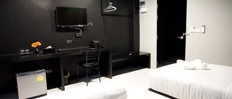 A modern hotel room with a bed, a desk, a chair, a TV, and a small trash bin.