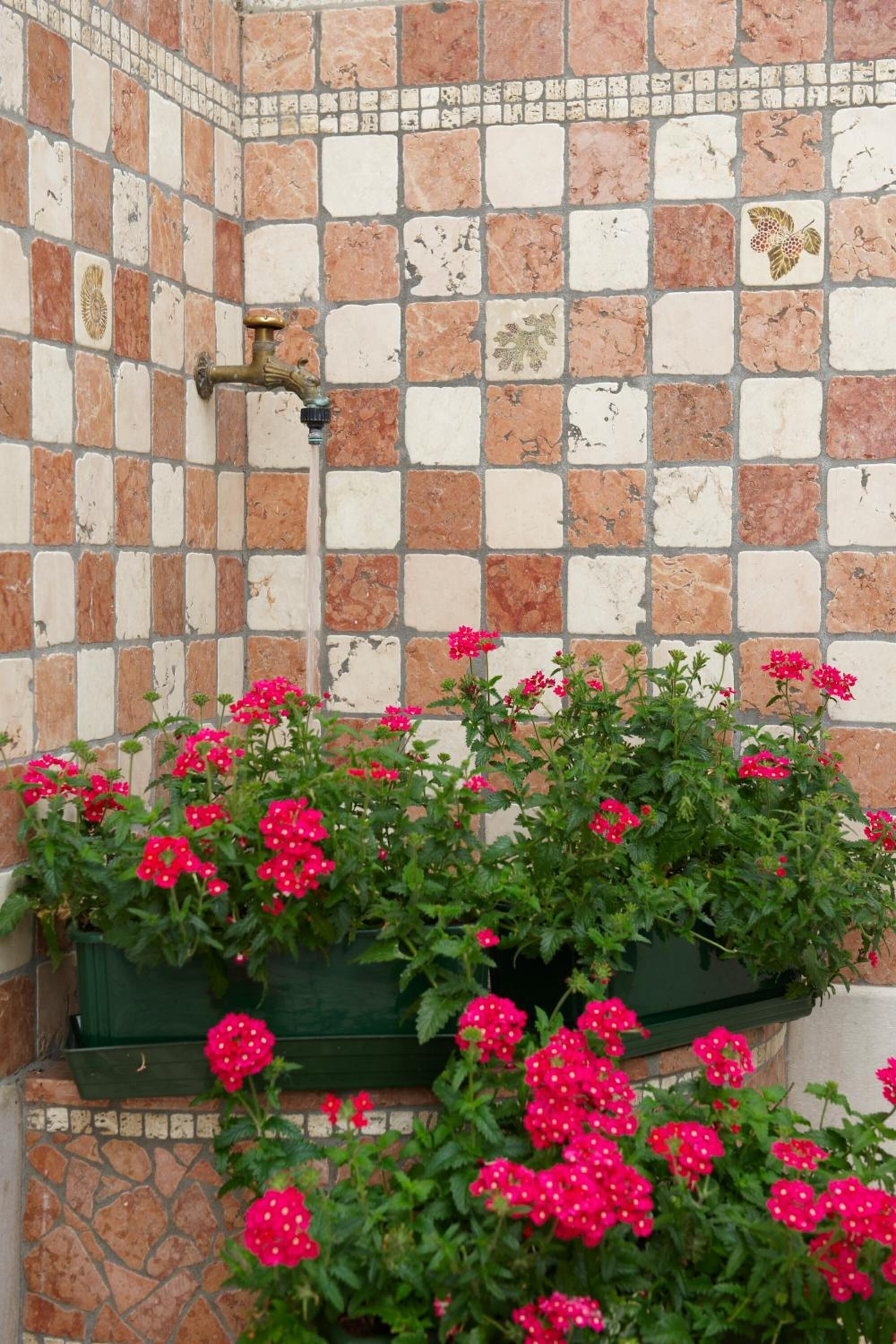 A tiled wall with a water spigot and a planter box with pink flowers.