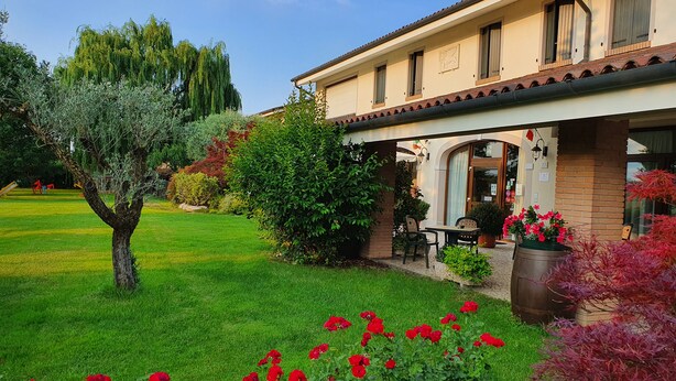 A two-story building with a covered patio area, a lawn, and a variety of plants and flowers. - Agriturismo Il Cascinale (Treviso)