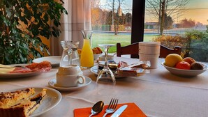 A breakfast table with plates of food, a pitcher of orange juice, and a view of a park. - Agriturismo Il Cascinale (Treviso)
