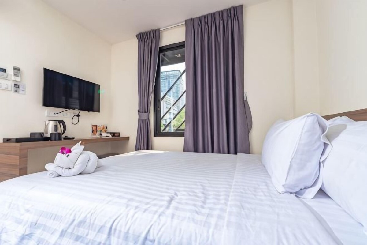 Une chambre d’hôtel équipée d’un lit, d’un téléviseur à écran plat, d’un bureau avec une machine à café et d’une fenêtre avec des rideaux.